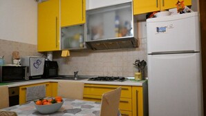 Een keuken met gele kastjes, een witte koelkast, een magnetron en een gasfornuis.