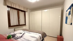 Een slaapkamer met een bed, een raam met gordijnen, een kledingkast en een schilderij aan de muur.