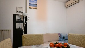 Een eethoek met een tafel, stoelen, een schaal fruit en wanddecoratie met stadsgezichten.