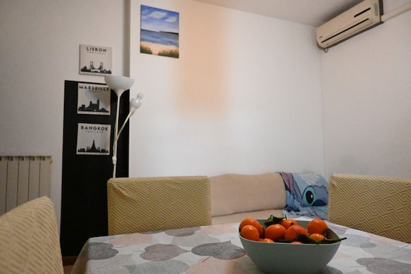 A dining area with a table, chairs, a bowl of fruit, and wall art depicting cityscapes.
