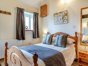 Une chambre à coucher avec un cadre de lit en bois, une fenêtre avec des rideaux, une table de chevet avec une lampe et un miroir fixé au mur.