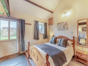 A bedroom with a wooden bed, a window with curtains, a bedside table with a lamp, and a painting on the wall.