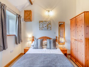 Ein Schlafzimmer mit einem Bett, zwei Nachttischlampen, einem Holzschrank, einem Gemälde und einem Fenster mit Vorhängen.