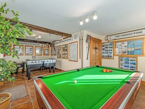 A pool table with a green felt surface, a foosball table, and a billiards cue rack.