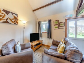 Un salon comprenant un ensemble de canapés, un téléviseur à écran plat posé sur un meuble en bois, une lampe sur pied et une fenêtre avec des rideaux.