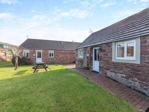 A brick building with a tiled roof, a small garden, and a picnic table. - Eight Byre - UK48913 (Allonby)
