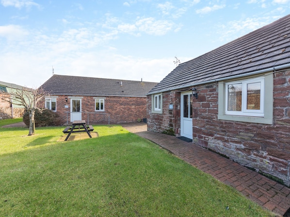 A brick building with a tiled roof, a small garden, and a picnic table.