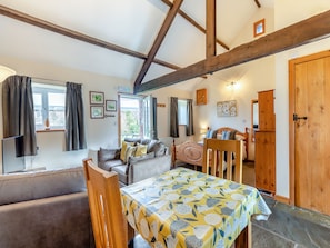 A cozy room with a wooden ceiling, a sofa, a dining table with a floral tablecloth, and a bed with wooden headboard. - Eight Byre - UK48913 (Allonby)