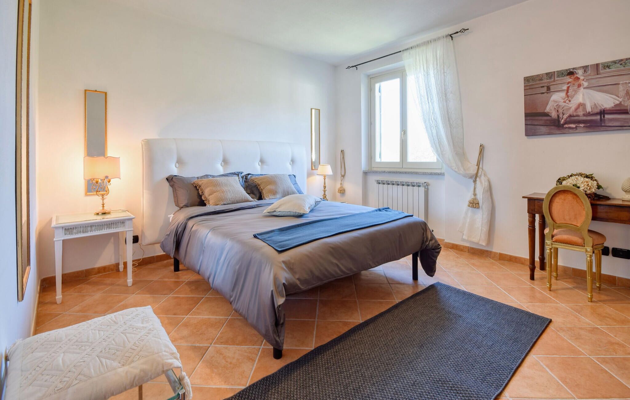 Een slaapkamer met een groot bed, een nachtkastje, een stoel, een bureau en een raam met gordijnen.