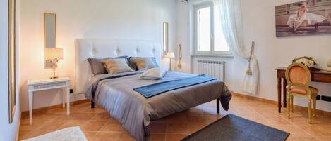 Een slaapkamer met een groot bed, een nachtkastje, een stoel, een bureau en een raam met gordijnen.