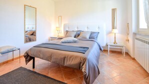 A bedroom with a large bed, two bedside tables, a nightstand, a mirror, and a window with curtains.