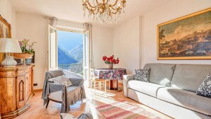 A living room with a sofa, a table with flowers, a chandelier, and a painting on the wall.