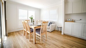A modern kitchen with white cabinets, a dining area with wooden chairs and a table, and a small side table.