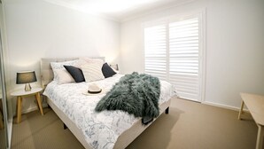 A bedroom with a bed, bedside tables, a lamp, and a window with blinds.