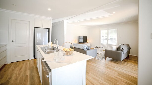 A modern kitchen with a central island, a dining area with a sofa, and a living room with a TV and seating.