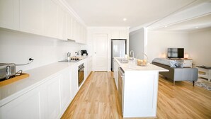 A modern kitchen with white cabinetry, a central island, and a dining area with a sofa and TV.