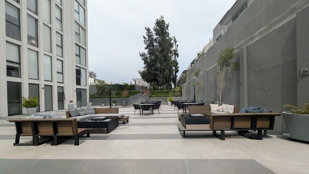 An outdoor seating area with modern furniture, a building with large windows, and a tree in the background. - Modern New Apartment Near Andares (Zapopan)