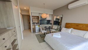 A hotel room with a bed, a desk, a chair, a small kitchenette, and a wardrobe. - Modern New Apartment Near Andares (Zapopan)