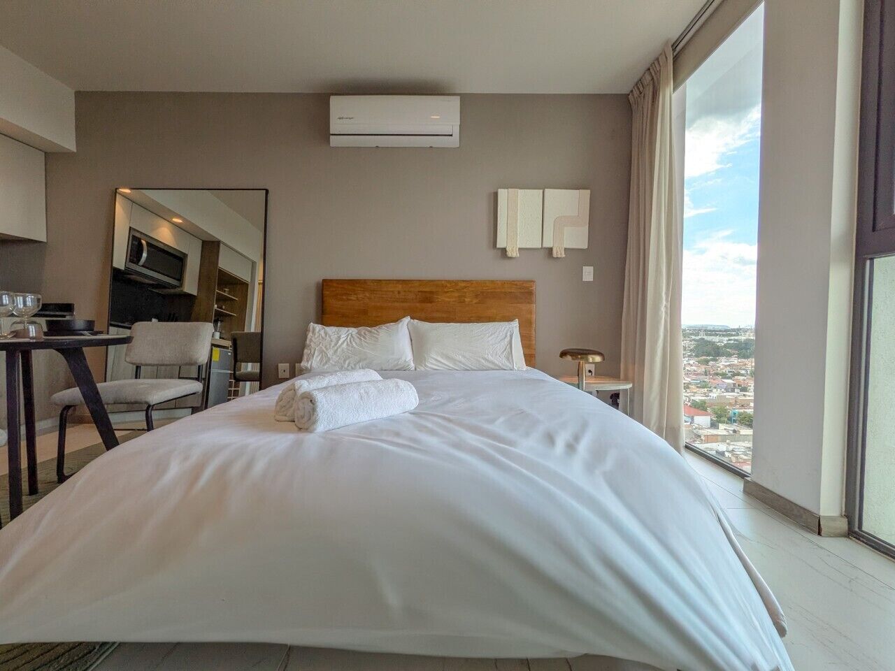 Hotellihuone, jossa on suuri sänky, työpöytä, tuoli, televisio ja näkymä kaupunkiin.