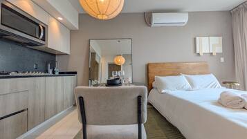 Ein Hotelzimmer mit Bett, Sessel, einer Küchenzeile, einem Spiegel und einer Klimaanlage.