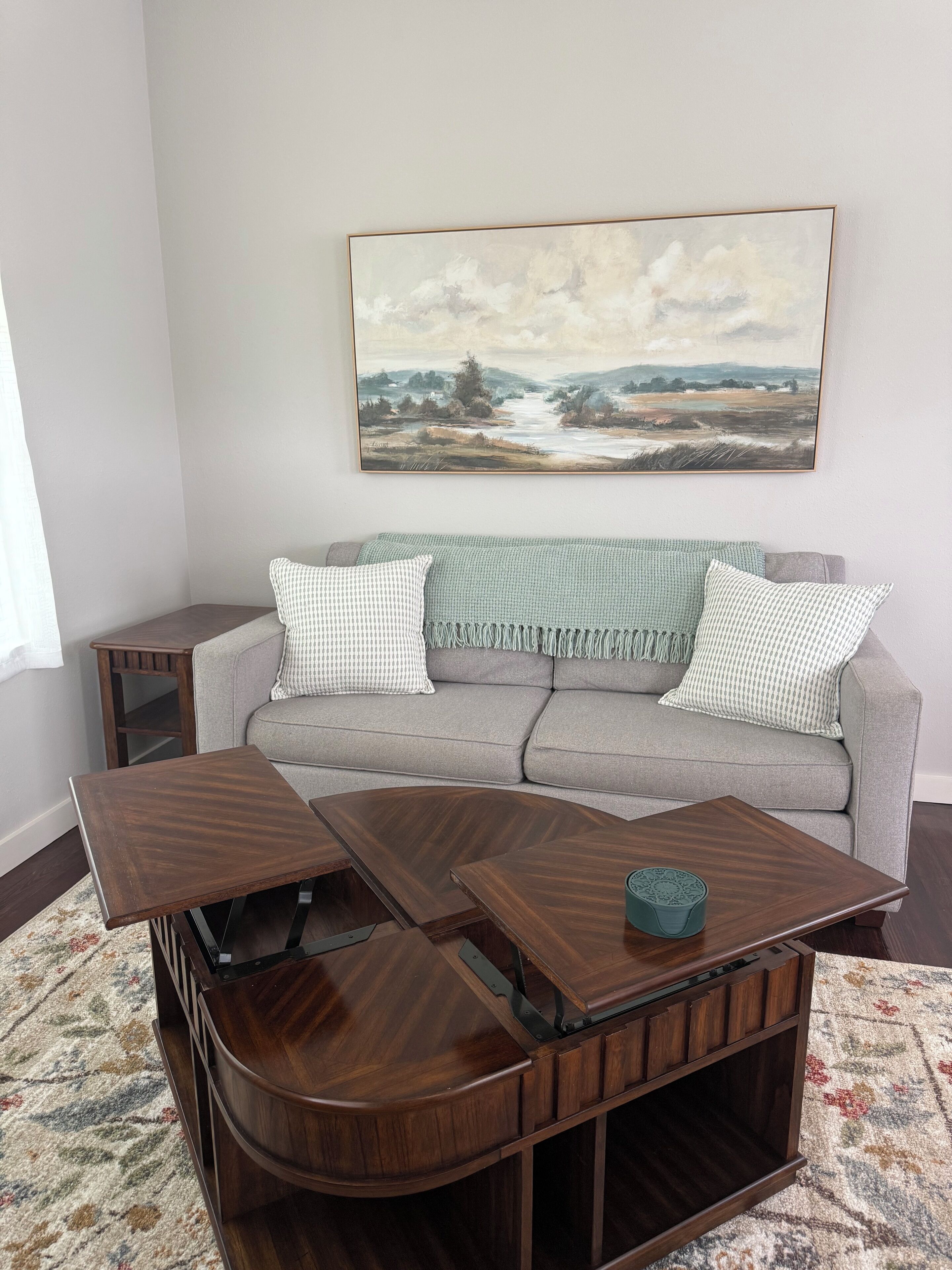 A living room with a grey sofa, two wooden coffee tables, and a painting on the wall.