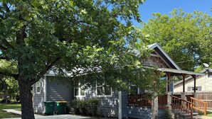 Una casa con porche cubierto, un gran árbol en el frente y un césped bien cuidado.