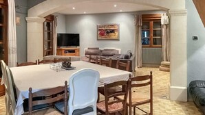 Una zona de menjador amb una taula gran, cadires, una televisió i un quadre a la paret.