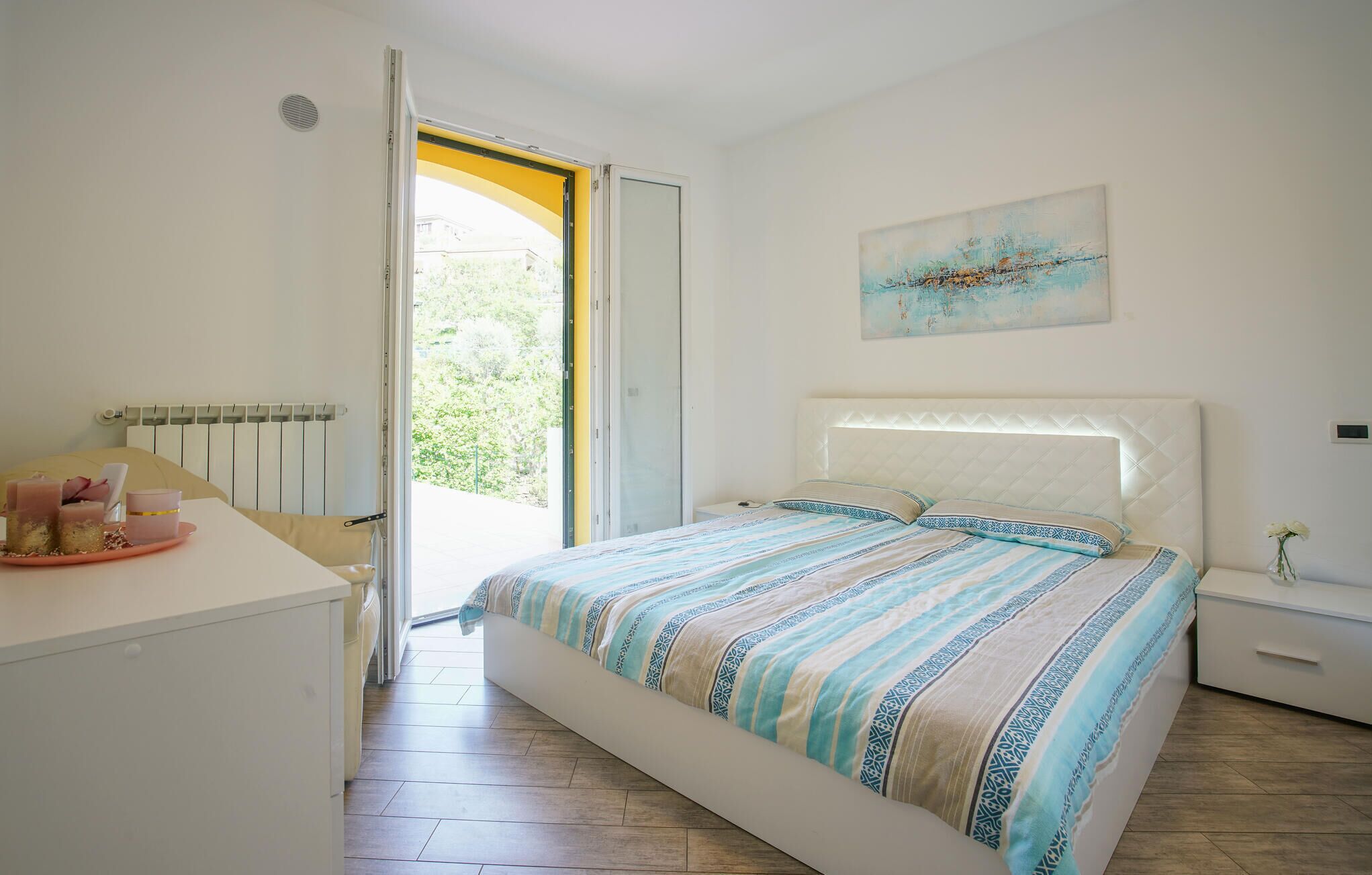 Een slaapkamer met een bed, nachtkastje, radiator en een raam met een open deur.