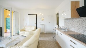 A modern kitchen with a wooden countertop and white cabinetry. There is a white sofa and a dining table in the living area. - 2 bedroom nice home in Imperia (Imperia)