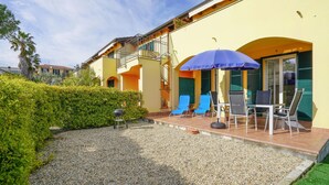 A yellow building with a balcony, outdoor seating with umbrellas, and a gravel patio. - 2 bedroom nice home in Imperia (Imperia)