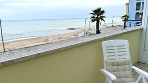 A balcony with a view of the beach, a white chair, and a building in the background. - P049 – Porto Recanati, comfortable studio apartment with sea view (Porto Recanati)