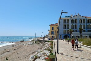 A coastal promenade with buildings, a beach, and a clear sky.