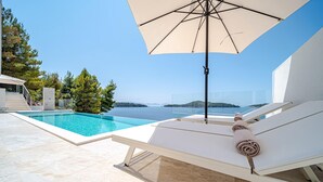 Un espace aménagé au bord de la piscine offrant une vue dégagée sur la mer, avec un fauteuil de relaxation et un grand parasol.