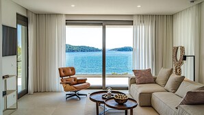 Un salon moderne doté d’une grande fenêtre donnant sur un lac et des collines.