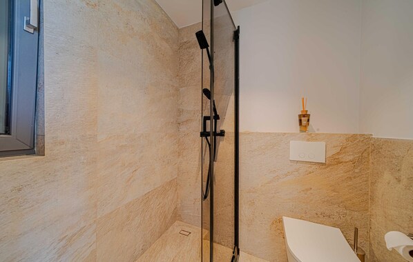 A modern bathroom with a glass-enclosed shower, a toilet, and a small shelf with a bottle and reed diffuser.