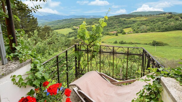A balcony with a view of a lush green landscape, a wooden chair, and red flowers. - Stunning home in Poggio d'Acona (Poggio d'Acona)