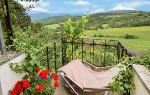 Un balcó amb vistes a un paisatge verd i exuberant, una cadira de fusta i flors vermelles.