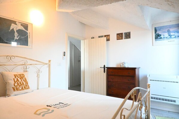 A bedroom with a bed, a dresser, a wall-mounted air conditioner, and a door leading to another room.
