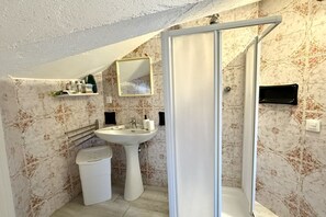 A bathroom with a pedestal sink, a toilet, a shower enclosure, a mirror, and a shelf with toiletries. - M416 – Marcelli, attic seen badly a few steps from the beach (Marcelli)