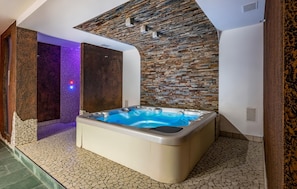 A spa area with a hot tub, stone walls, and a tiled floor.