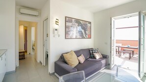 Una sala de estar moderna con un sofá gris, una mesa de centro de vidrio, un cuadro en la pared y una puerta que da a un balcón.