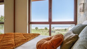A bedroom with a large window offering a view of the beach and ocean.