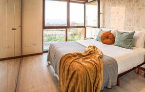 Un dormitorio con un ventanal grande, una cama con muchas almohadas y una manta en el suelo.