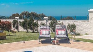 A patio with two lounge chairs, a small table, and a view of the sea.