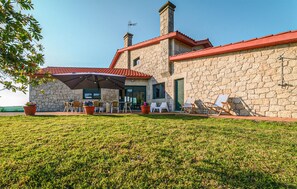 Un edificio de piedra con techo de tejas rojas, zona de estar al aire libre con sillas y una mesa, y un césped.