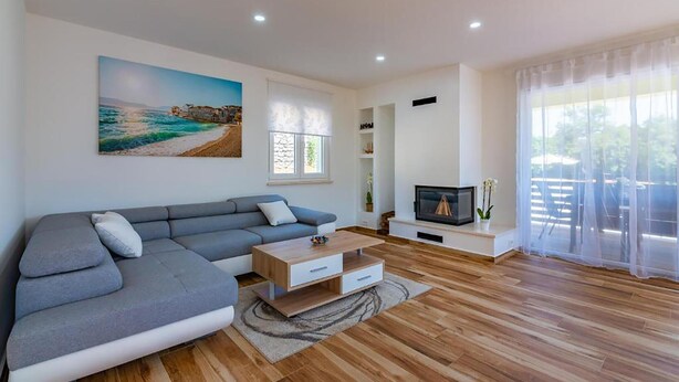 A modern living room with a grey sectional sofa, a wooden coffee table, a TV on a stand, and a large window with sheer curtains. - Amazing home in Matulji (Matulji)