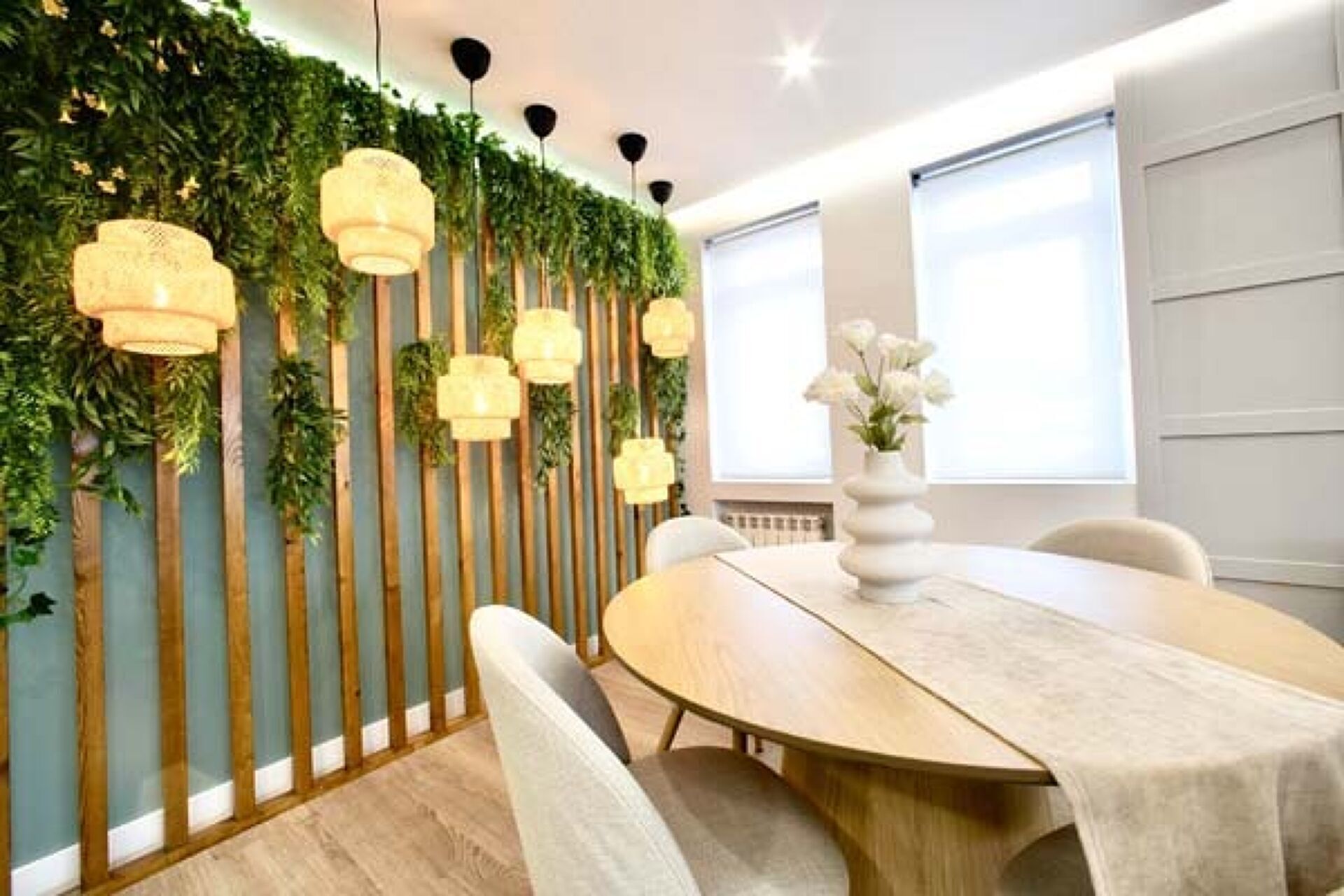 Un comedor moderno con una mesa redonda, sillas blancas y una pared decorativa con listones verticales de madera y luces colgantes.