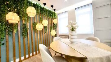Un comedor moderno con una mesa redonda, sillas blancas y una pared decorativa con listones verticales de madera y luces colgantes.