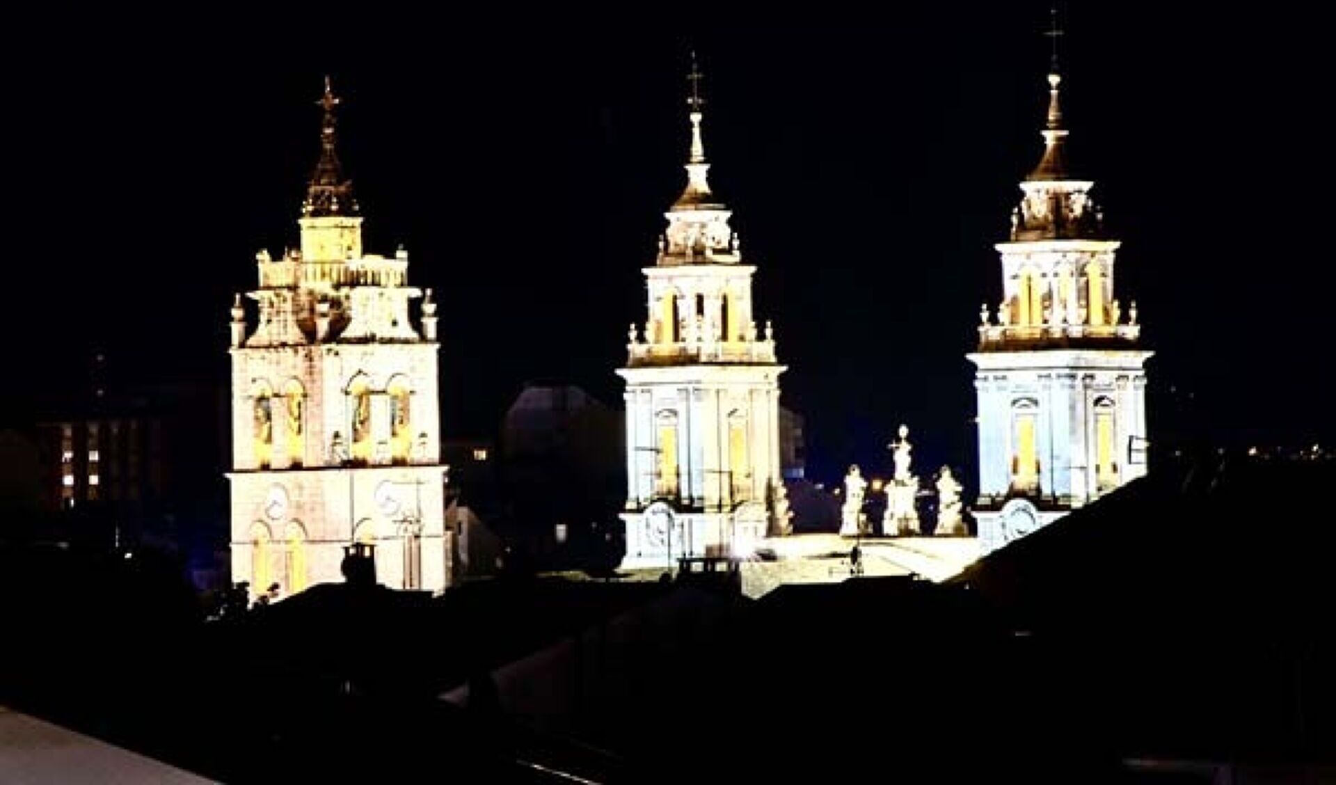 Vista nocturna de un edificio histórico con tres torres iluminadas.