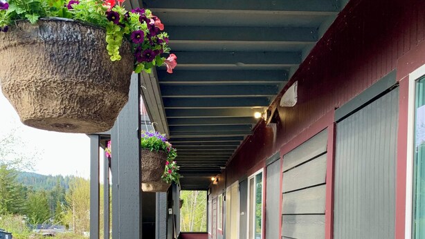 A covered porch with wicker furniture, hanging flower baskets, and a view of the road. - Hidden JEM Apartment-Hotel - Spacious Home Away From Home (Coal Harbour)